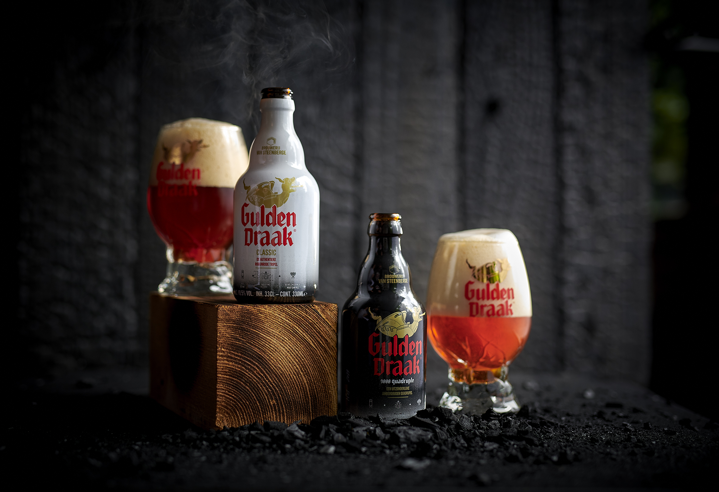 Gulden Draak bottles and glasses lit against a dark backdrop